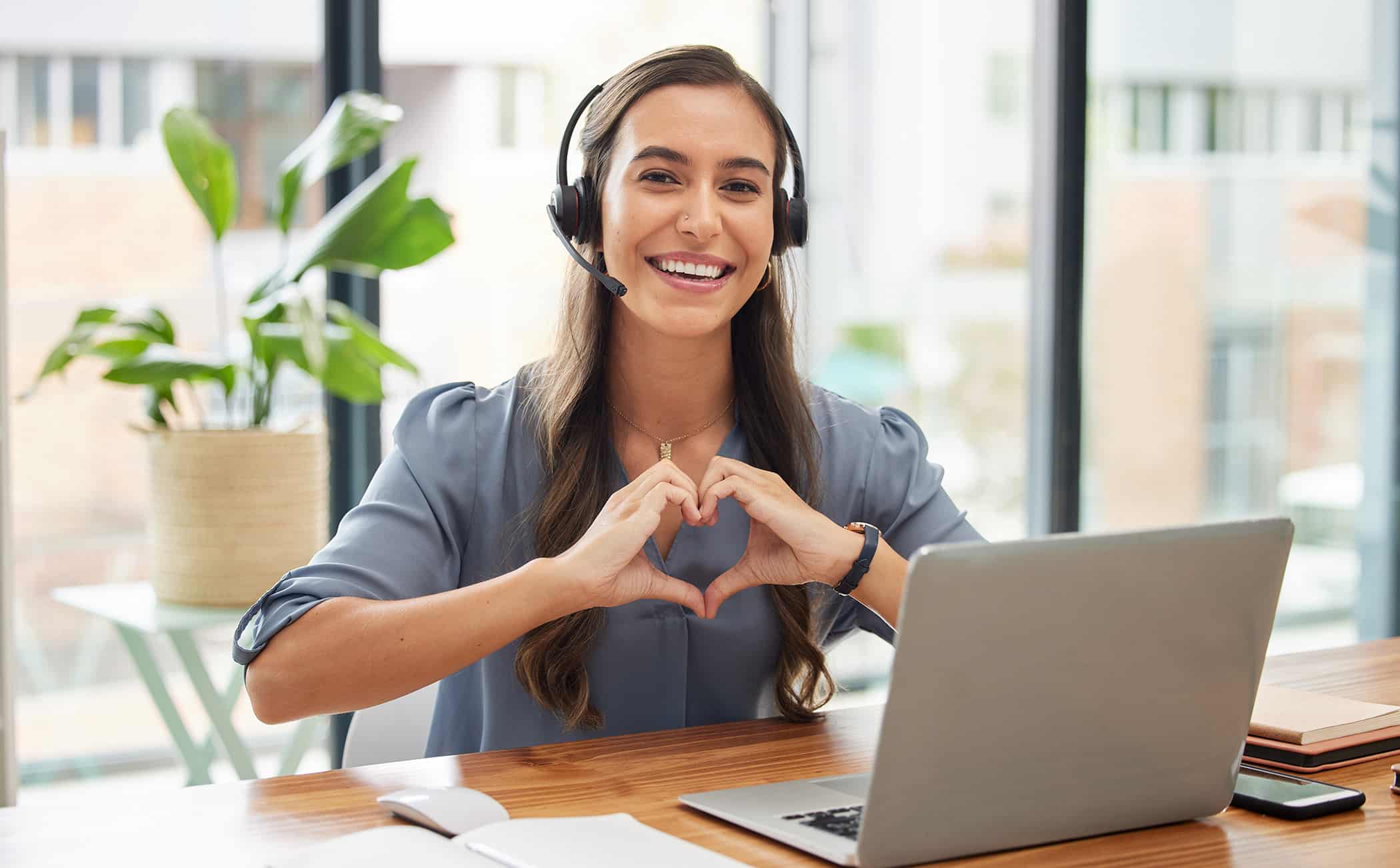 Woman, call center and laptop with heart gesture for telemarketing, customer service or support at the office. Portrait of happy employee consultant with smile and hands with love symbol by computer.