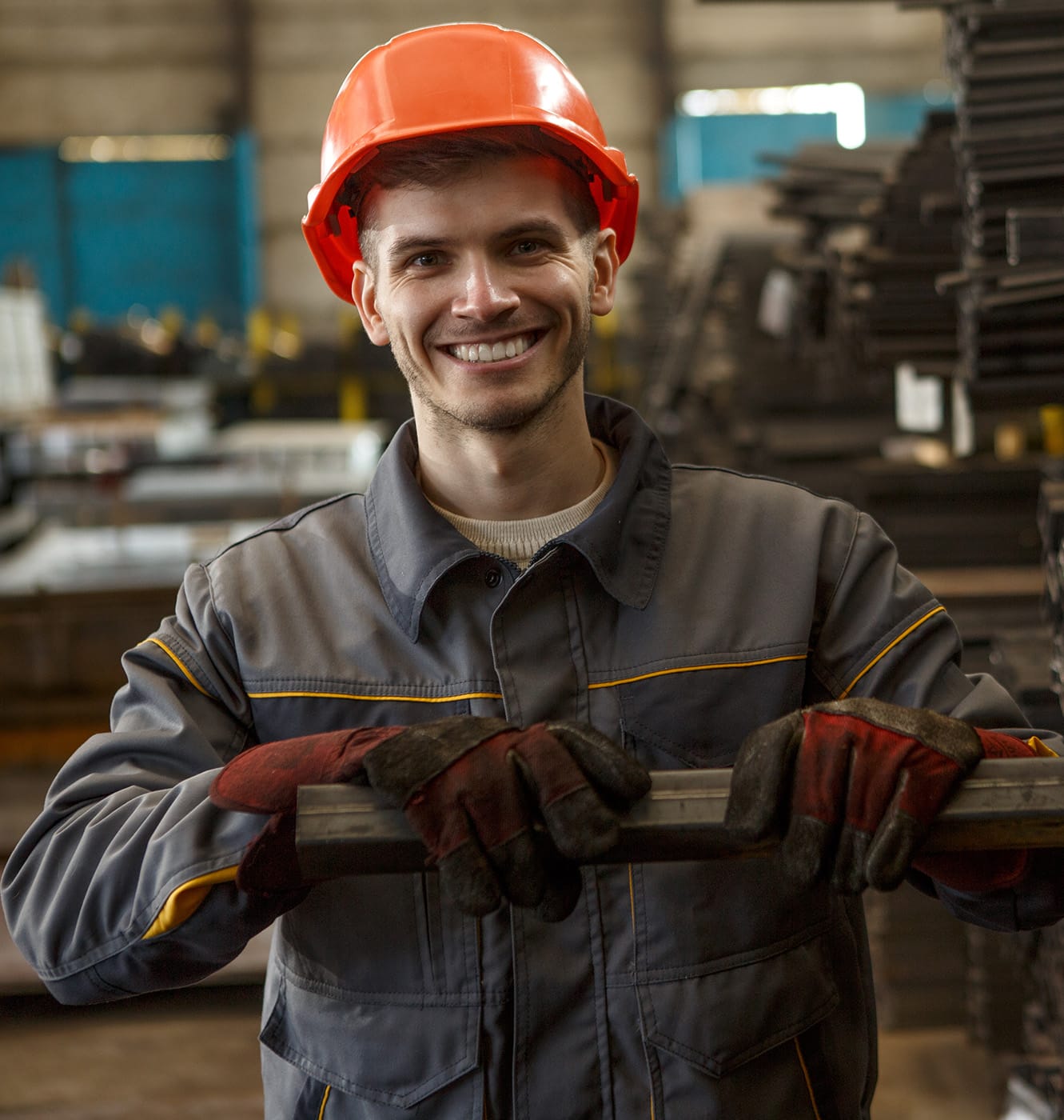Portrait of happy worker in gray uniform, orange helmet and protective suit standing hear metal tubes.